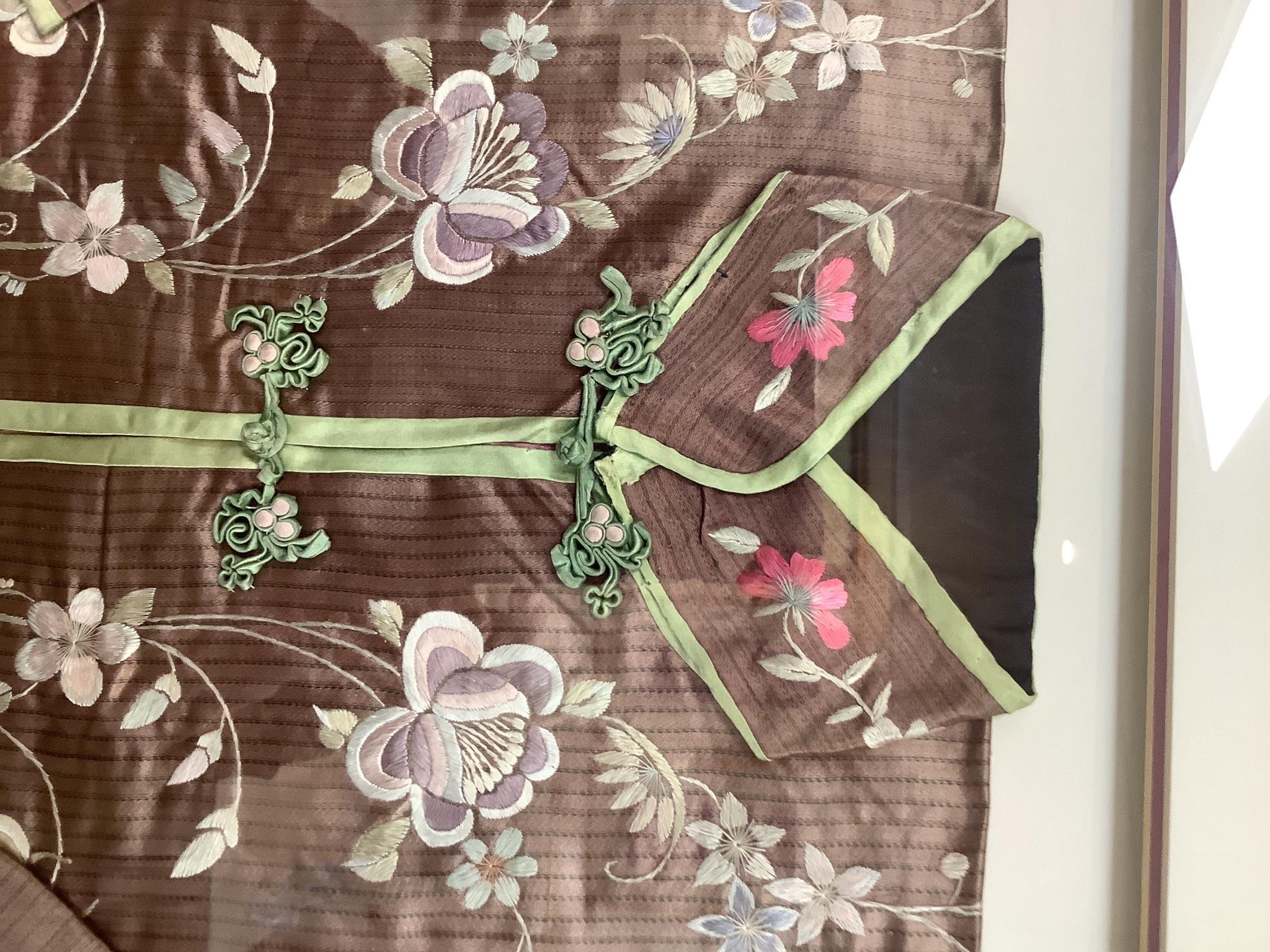 An early 20th century Chinese brown silk robe, with pastel multi-coloured all over embroidered flowers, framed and double mounted, measured as mounted: 75cm wide, 61cm high